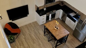 A modern kitchen with a dining area, a flat-screen TV, and a cozy seating area with a sofa and cushions. - Brand New Custom Built Cottage in Downtown w/Pool (Salem)