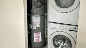 A compact laundry area with a stacked washer and dryer, a water heater, and visible electrical outlets. - Brand New Custom Built Cottage in Downtown w/Pool (Salem)