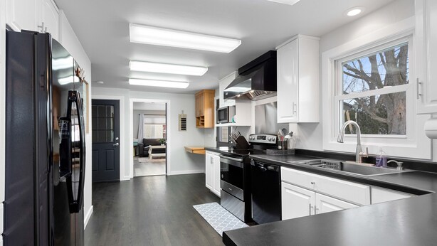 A modern kitchen with dark wood flooring, white cabinetry, and stainless steel appliances. - Very spacious, clean and tastefully remodeled home (Green Bay)