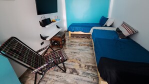 Una stanza piccola e funzionale con un letto, una sedia, una scrivania con un computer e una TV a parete.