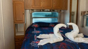 A bedroom with a bed, wooden cabinets, and a window with a view of the sea. - San Blas RV Park Frente al Mar (San Blas)