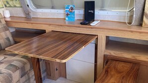 A compact RV interior with a wooden table, bench, and a window with blinds. - San Blas RV Park Frente al Mar (San Blas)