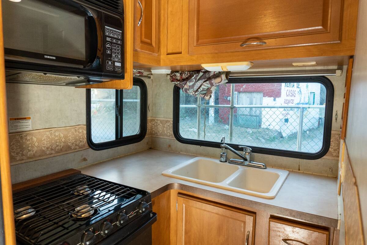 A compact kitchen with a microwave, stove, sink, and wooden cabinets.