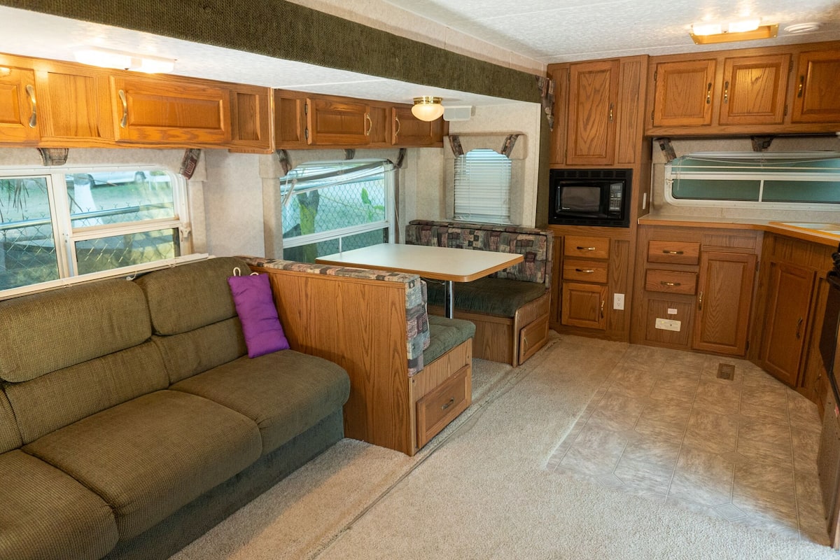 A compact RV kitchen with wooden cabinets, a microwave, and a small dining area.