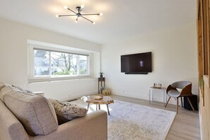 A modern living room with a large window, a flat-screen TV, a sofa, a coffee table, and a chair.