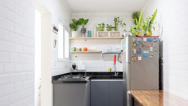 Una cocina compacta con paredes de azulejos blancos, un refrigerador de acero inoxidable y encimeras de madera.