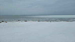 A snowy beach with a calm sea and overcast sky. - Motel Au Bord de l'eau (Rimouski)