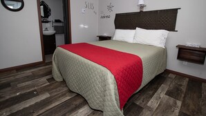 A bedroom with a bed, a nightstand, a bedside table, a wall-mounted lamp, and a mirror. - Motel Au Bord de l'eau (Rimouski)