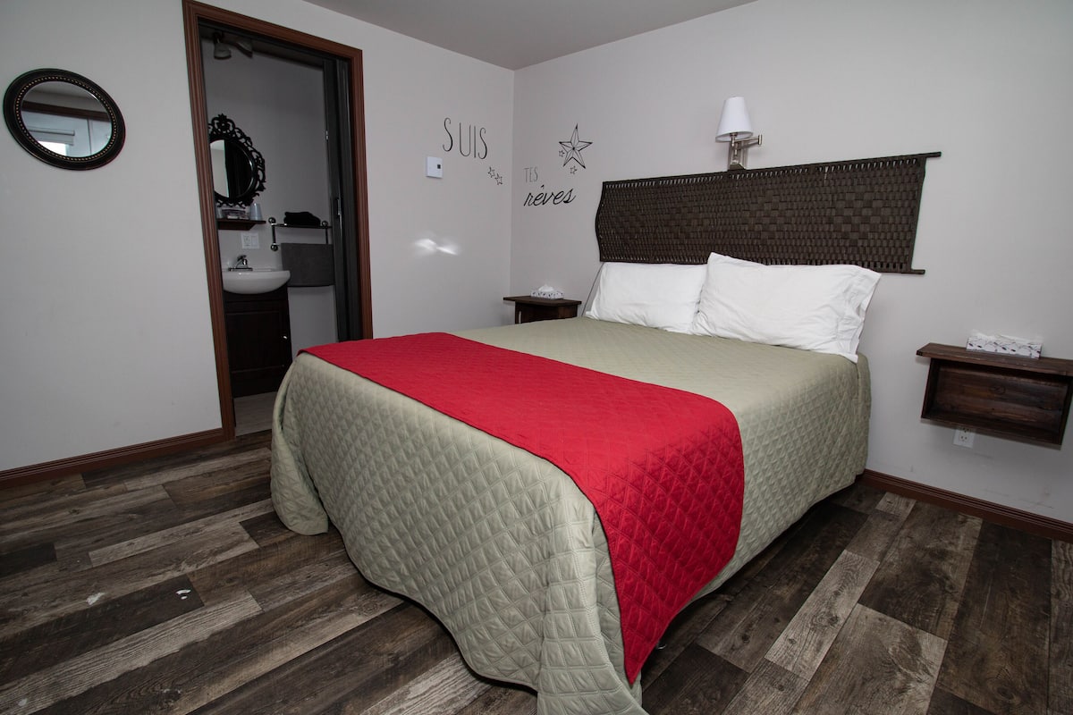 Ein Schlafzimmer mit einem Bett, einem Nachttisch, einer Wandlampe und einem Spiegel.