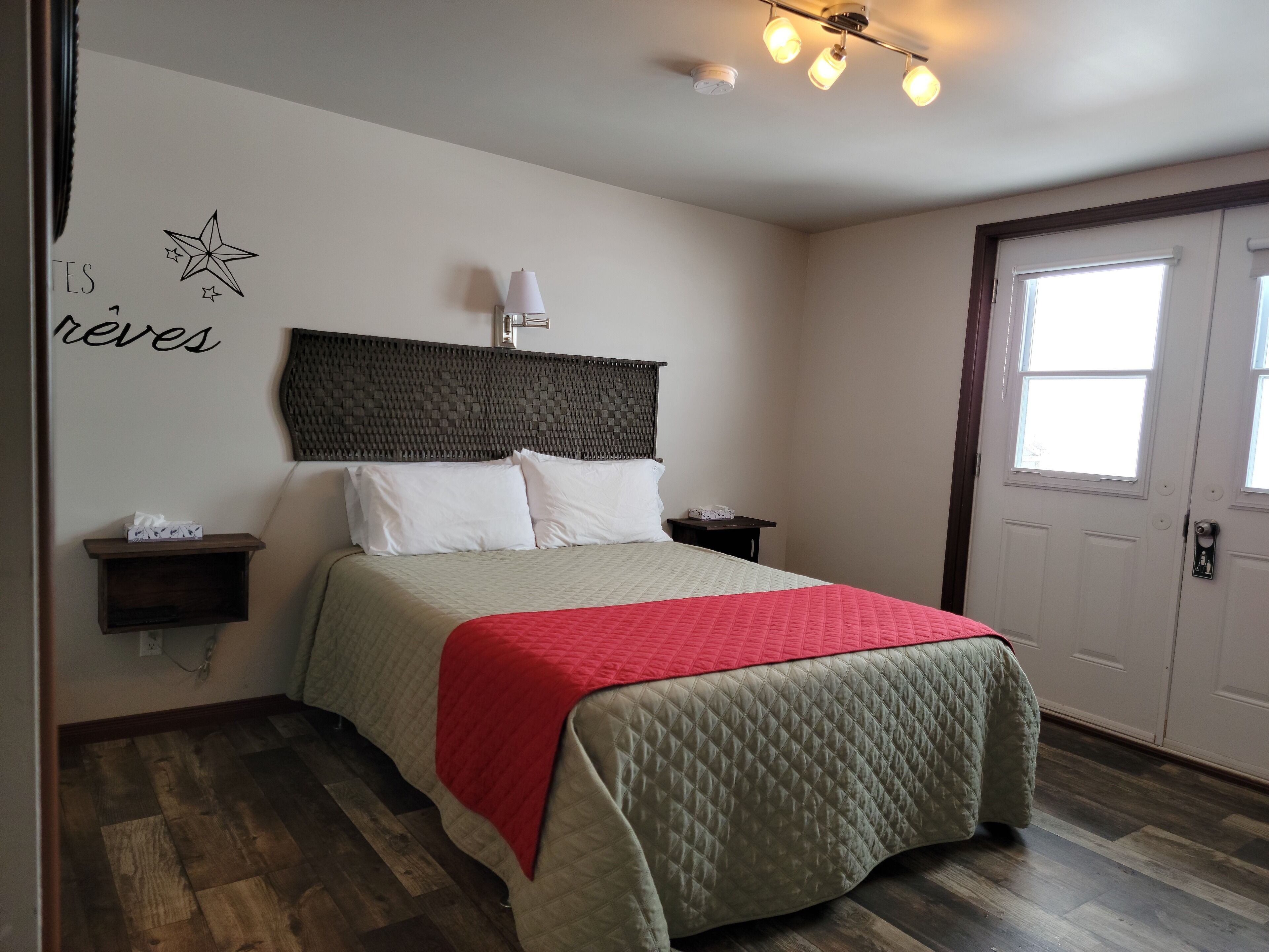 A bedroom with a bed, bedside tables, a wall-mounted lamp, and a door with windows.