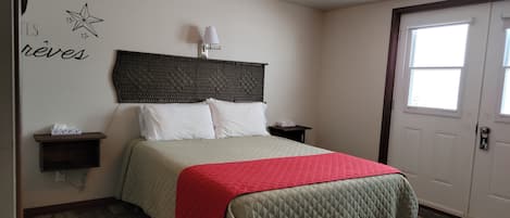 A bedroom with a bed, bedside tables, a wall-mounted lamp, and a door with windows.