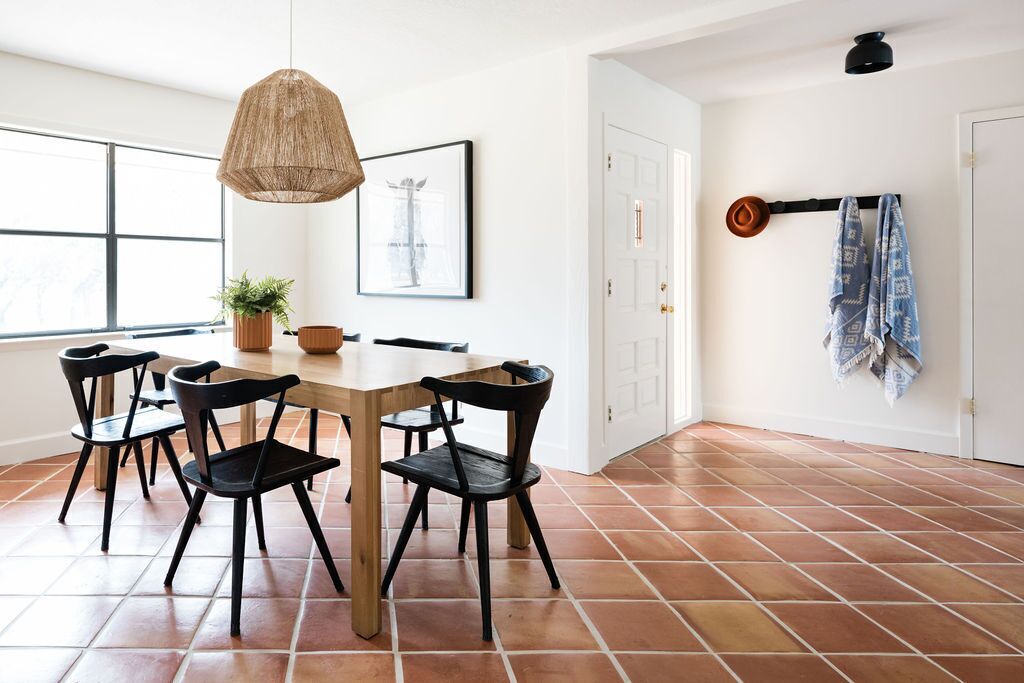Un coin repas avec une table en bois et des chaises noires, un luminaire suspendu et une plante en pot.