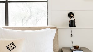 Une chambre à coucher avec un lit, une table de chevet avec une lampe, un tableau encadré et une fenêtre avec des stores.