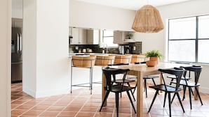 Une cuisine moderne avec un coin repas, dotée d’une grande fenêtre, d’un luminaire suspendu et d’un sol carrelé.