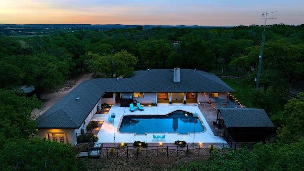 Une grande maison avec une piscine, entourée d’arbres et sous un ciel dégagé.