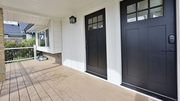 Un porche abrité avec une terrasse en bois, deux portes noires et une petite fenêtre.