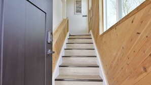 Un escalier en bois, avec une porte sombre sur la gauche et une fenêtre sur la droite.