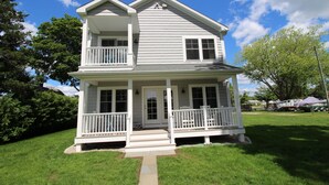 Une maison à deux étages avec un porche à l’avant, un balcon à l’étage supérieur et un petit jardin devant la maison.