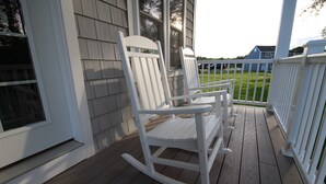 Une véranda avec deux fauteuils à bascule et une balustrade blanche.
