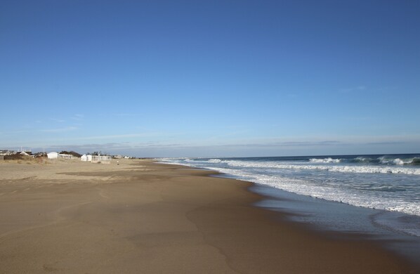 A beach with a sandy shore, a few white structures, and a clear blue sky.