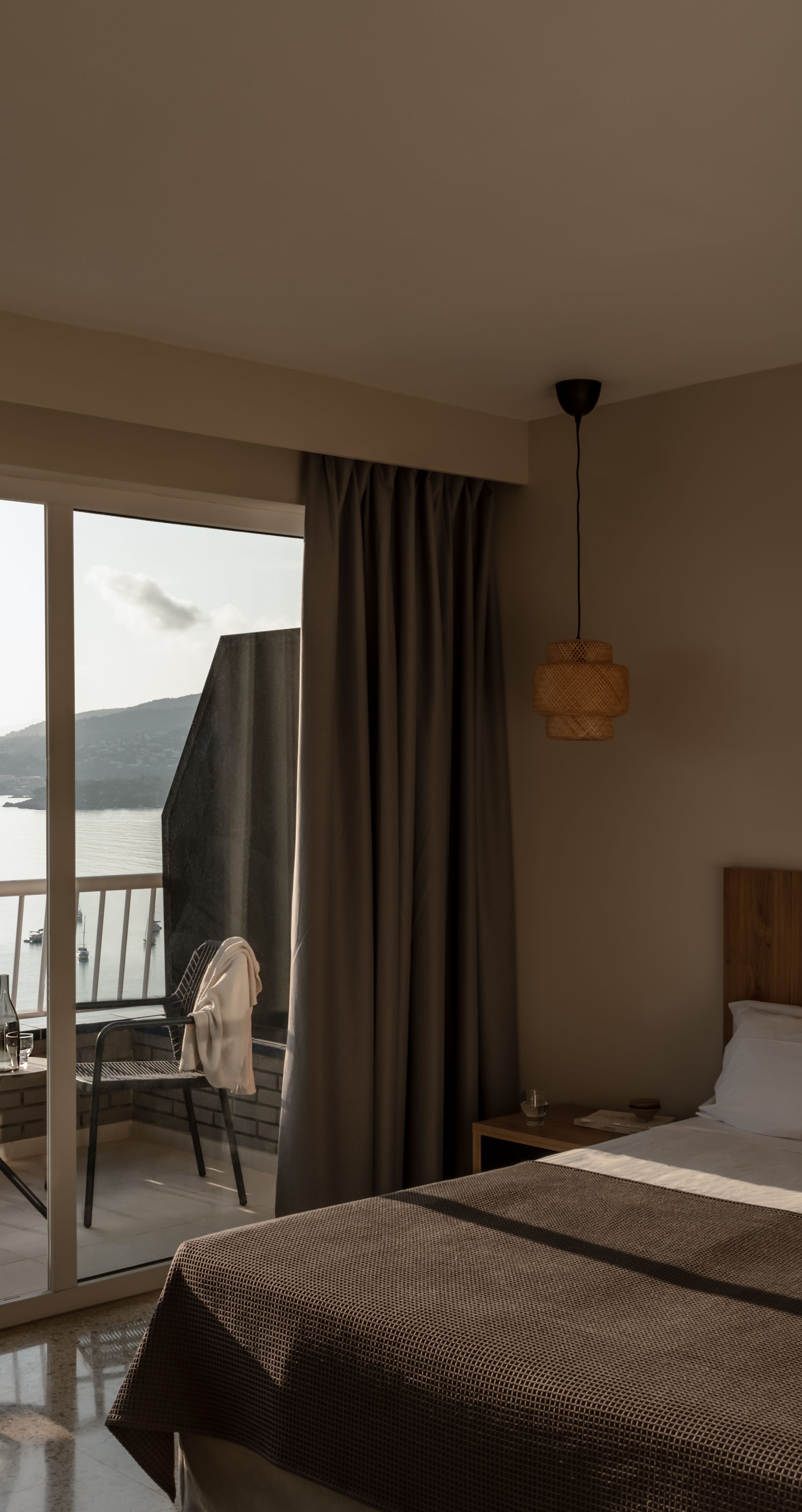 Een slaapkamer met een groot bed, een nachtkastje, een stoel en uitzicht op zee.