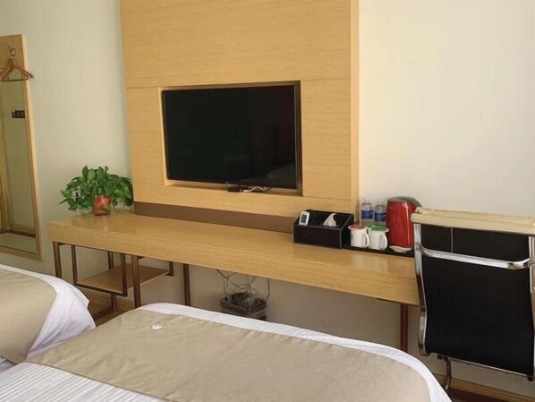 Une chambre d’hôtel avec un lit, un bureau avec une télévision, une plante et une machine à café.