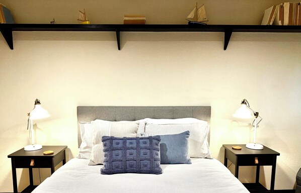 A neatly made bed with a grey headboard, two bedside tables with lamps, and a shelf above the bed with decorative items.