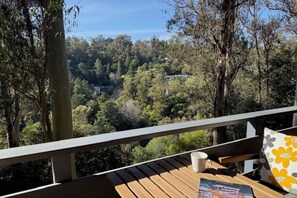 A wooden deck with a railing, a table, a chair, and a view of a forested area.