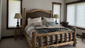 Ein Schlafzimmer mit einem Holzbettgestell, zwei Nachttischen und einem großen Fenster mit Jalousien.