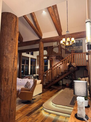 A spacious living area with a wooden staircase, a chandelier, and a fireplace. - Modern Chalet on the River. Hot Tub, Fireplace , Newly furnished Fishing, Hiking (Eagle)