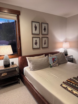 Quarto com cama, mesas de cabeceira, luminárias e quadros na parede.