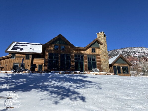 A wooden cabin with large windows and a stone chimney, surrounded by snow.