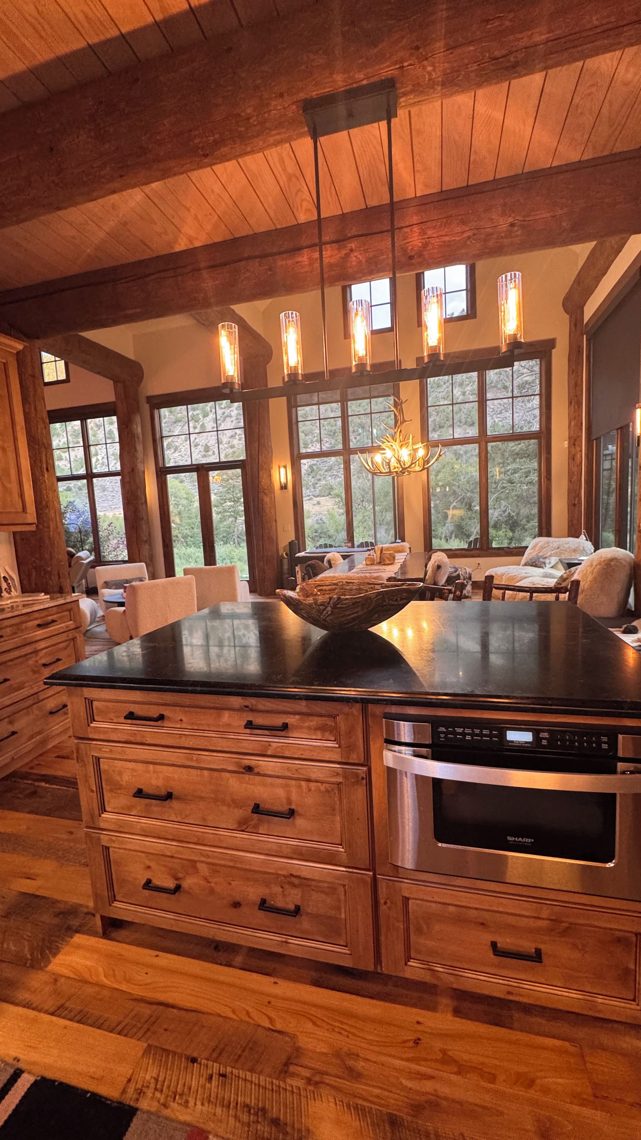 Cocina con muebles de madera, horno empotrado y comedor con un amplio ventanal que da a zonas verdes.