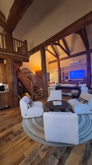 A spacious living area with a wooden staircase, a round coffee table, and a large flat-screen TV. - Modern Chalet on the River. Hot Tub, Fireplace , Newly furnished Fishing, Hiking (Eagle)