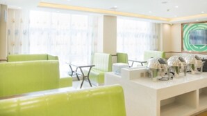 Un moderno vestíbulo de hotel con asientos verdes, una recepción y un ventanal con cortinas.