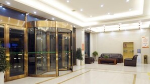 Un vestíbulo con puerta giratoria, mostrador de recepción, un sofá y una planta en maceta.