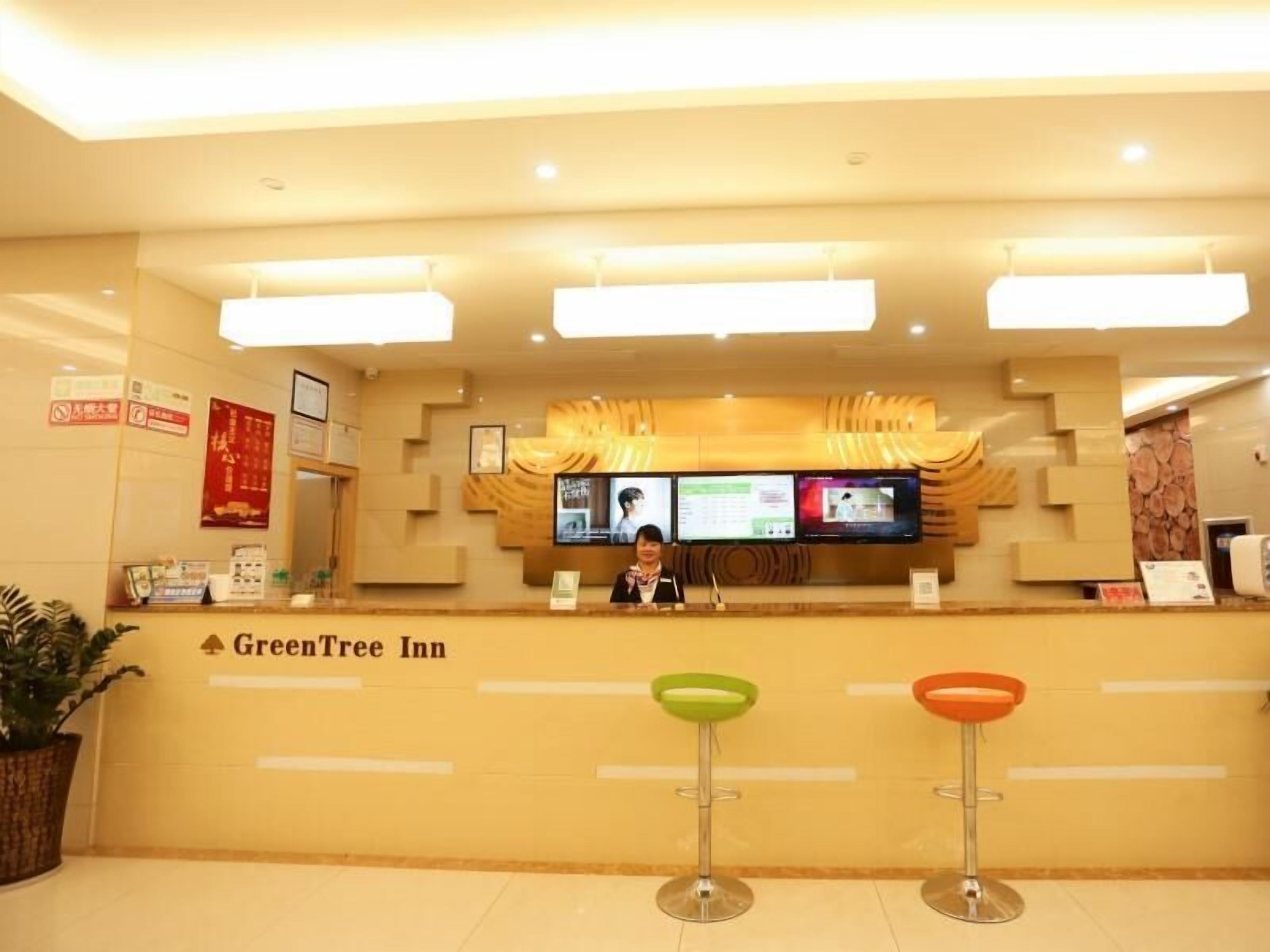 A reception area with a digital screen, a receptionist, and two stools.
