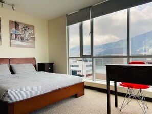 Une chambre avec un grand lit, un bureau et une fenêtre donnant sur la ville.