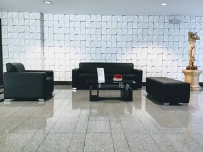 Un hall d’entrée avec un canapé noir, deux fauteuils, une table basse et une statue.