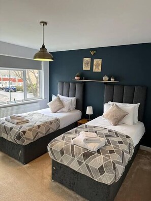 A hotel room with two beds, a window with a view of the street, and a shelf with decorative items.