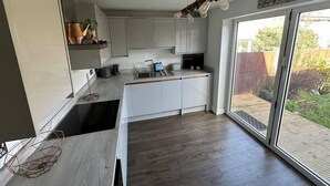 A modern kitchen with white cabinets, a wooden countertop, and a built-in oven. There is a window providing a view of the backyard. - Charming 2-BR House offering WIFI, Parking and a Garden | On Site Stays Welling (Welling)