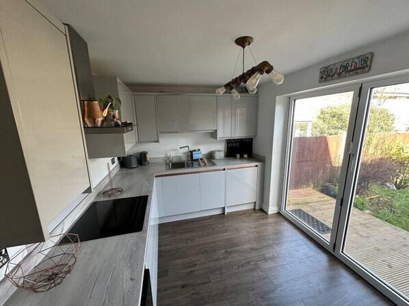 A modern kitchen with white cabinets, a wooden countertop, and a built-in oven. There is a window providing a view of the backyard.