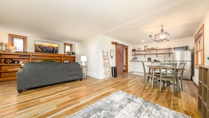 Ein großzügiger Wohnbereich mit grauem Sofa, Holzboden, einem Esstisch mit Stühlen sowie einer Küchenzeile mit Mikrowelle und Kühlschrank.
