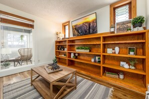 A cozy living room with a wooden bookshelf, a dining table, and a large window with blinds. - New! Lovely 1BR. Walk to Main St (Montrose)