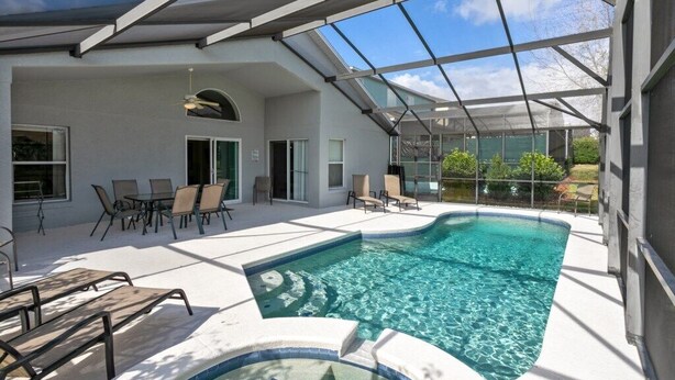 A modern indoor swimming pool with clear water, surrounded by lounge chairs and a glass-enclosed patio area.