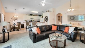 A modern living room with a black leather sofa, a glass coffee table, and a dining area with wicker chairs.