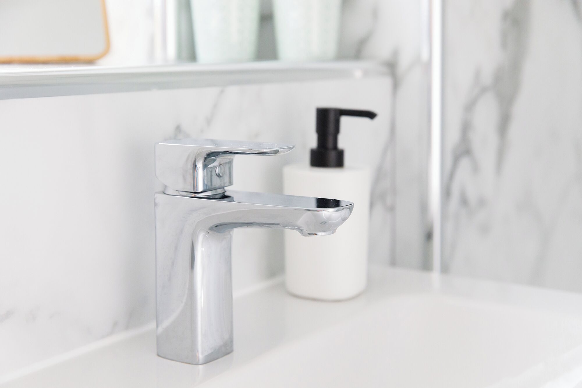 Un grifo cromado sobre un lavabo blanco con un salpicadero de mármol.