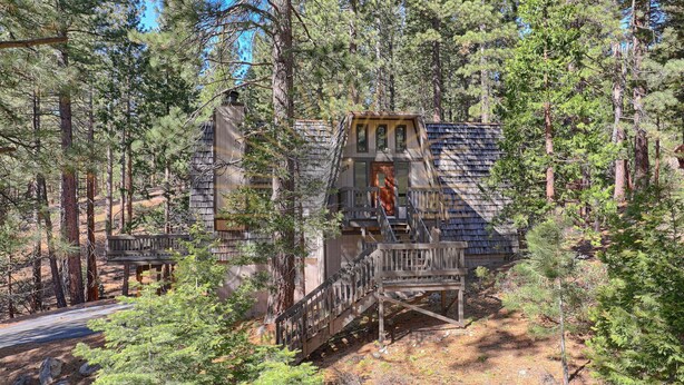 Une cabane rustique dotée d’une terrasse en bois et d’un escalier menant à une porte, le tout entouré d’une forêt dense.