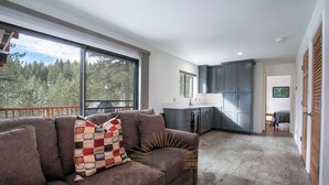 Un salon moderne doté d’une grande fenêtre, d’un canapé marron et d’un coin cuisine avec des meubles de couleur sombre.