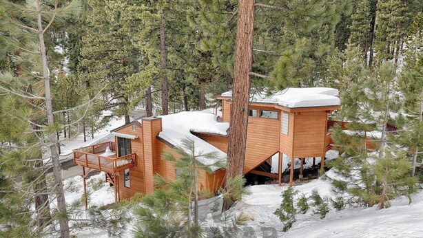 Une cabane en bois dotée d’un balcon, entourée de pins et recouverte de neige.